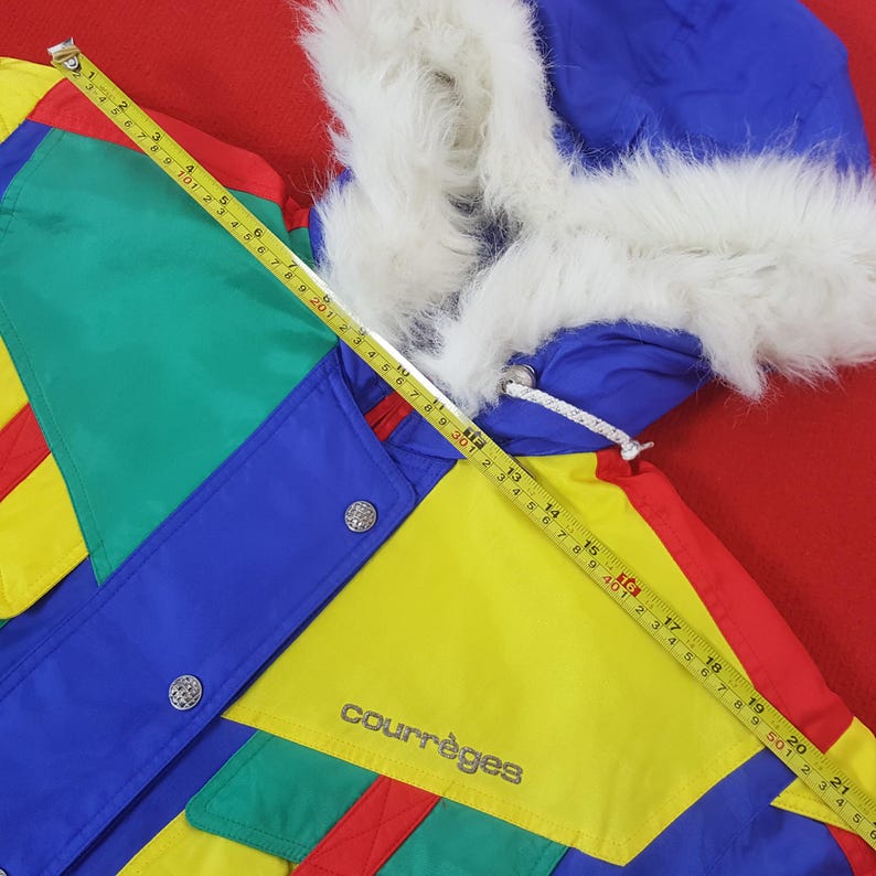 Puede incluir: Una colorida chaqueta Courr&egrave;ges vintage con una capucha ribeteada con piel sint&eacute;tica blanca. La chaqueta presenta un vibrante dise&ntilde;o de patchwork en azul, verde, amarillo y rojo. La chaqueta tiene botones plateados y el logo de Courr&egrave;ges.