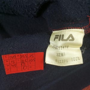 May include: A navy blue fleece jacket with a red zipper and a white FILA label. The label has the text "FILA", "FFAGX3478", "法定表示", and "ポリエステル 100%".