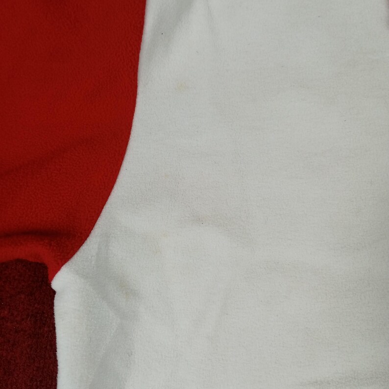 May include: Close-up of a white fleece fabric with a red fleece fabric seam. The white fabric has a soft, fuzzy texture.