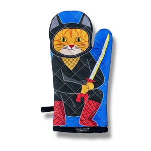 May include: A blue oven mitt with a quilted design features a cartoon orange cat dressed as a ninja holding a sword. The cat is wearing a black ninja suit with a yellow mesh mask and red boots. The text "NAKED DECOR" is printed on the bottom of the mitt.