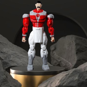 Op de afbeelding: Een rood, wit en grijs actiefiguur van een gespierd personage met een snor. Het figuur heeft een rode torso met witte en grijze accenten, een witte broek en grijze laarzen. Het staat op een goudkleurig platform.