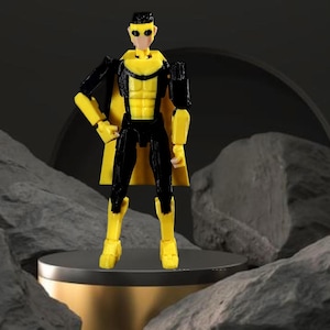 Op de afbeelding: Een geel en zwart actiefiguur van een superheld met een gele cape. Het figuur staat op een goud en grijs platform. De superheld heeft een geel masker, borst, laarzen en handschoenen. De rest van het figuur is zwart.