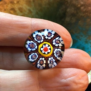 May include: A round glass bead with a multi-coloured floral pattern. The bead has a white background with red, yellow, blue, and brown flowers.
