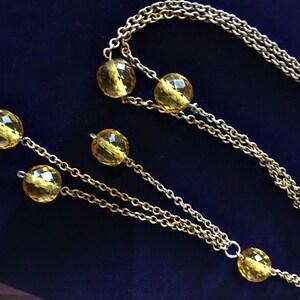 May include: A gold-toned necklace with faceted yellow beads. The necklace features a long chain with multiple strands and decorative beads. The beads are evenly spaced along the chain, creating a classic and elegant look.