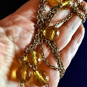 May include: A vintage necklace featuring faceted amber-colored glass beads and a gold-toned chain. The beads are round and have a sparkling, cut-glass appearance. The chain is made of small, interlocking links, creating a classic and elegant design.