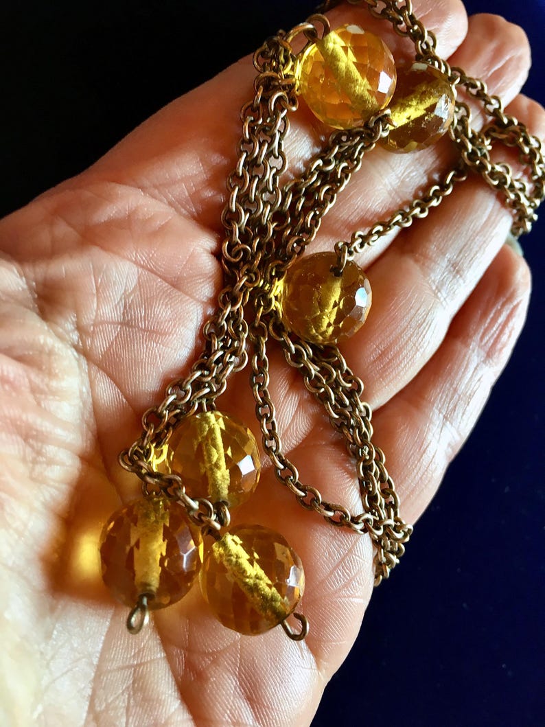 May include: A vintage necklace featuring faceted amber-colored glass beads and a gold-toned chain. The beads are round and have a sparkling, cut-glass appearance. The chain is made of small, interlocking links, creating a classic and elegant design.