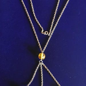 May include: A gold-colored necklace with a delicate chain design. The necklace features multiple strands and is adorned with yellow, faceted beads. The beads are evenly spaced along the chain, creating a symmetrical and elegant look. The necklace is displayed against a dark blue background.