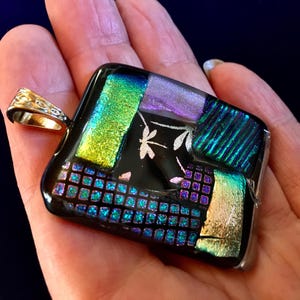Könnte beinhalten: Quadratischer Glasanhänger mit schwarzem Hintergrund und einem Mosaik aus irisierenden grünen, violetten und blauen Glasstücken. Der Anhänger zeigt ein Design mit einer silbernen Libelle und Blättern.