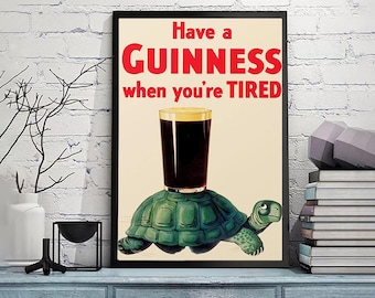 Op de afbeelding: Een vintage poster met een zwart frame die reclame maakt voor Guinness bier. De poster toont een groene schildpad die een glas Guinness draagt met de tekst "Have a GUINNESS when you're TIRED".