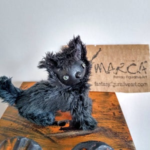 Può includere: Figurina di gatto in peluche nero con occhi verdi. Il gatto è in piedi su una superficie di legno con vernice arancione e marrone. Lo sfondo è bianco. La figurina è etichettata "MARCA" con il testo "Fantasy Figurative Art" e il sito web "fantasyfigurativeart.com".