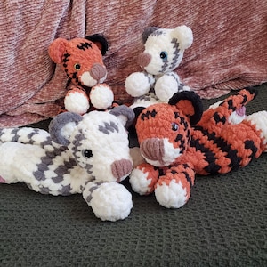 May include: Four handmade crochet tiger plush toys in various poses. Two are orange and black striped, one is white with gray spots, and the other is white with gray stripes. All have white paws, brown noses, and black ears.