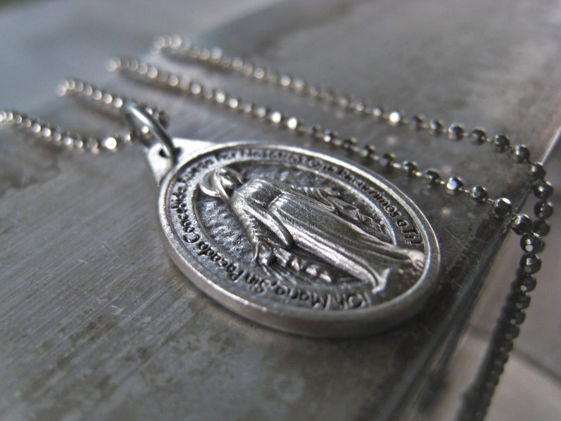 Puede incluir: Collar de cadena de plata con un colgante de plata que representa a la Virgen Mar&iacute;a. El colgante tiene la inscripci&oacute;n "Nuestra Se&ntilde;ora del Perpetuo Socorro" alrededor del borde.