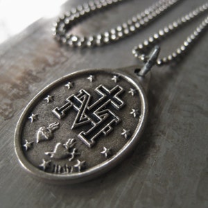 Puede incluir: Un collar de cadena de plata con un colgante de plata que presenta un dise&ntilde;o de cruz estilizado con un coraz&oacute;n y llamas. El colgante tiene forma ovalada y presenta un dise&ntilde;o detallado.
