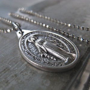 Puede incluir: Collar de cadena de plata con un colgante de plata que representa a la Virgen Mar&iacute;a. El colgante tiene la inscripci&oacute;n "Nuestra Se&ntilde;ora del Perpetuo Socorro" alrededor del borde.