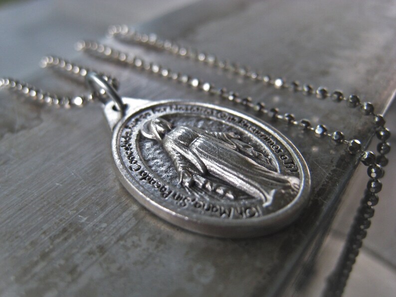 Puede incluir: Collar de cadena de plata con un colgante de plata que representa a la Virgen Mar&iacute;a. El colgante tiene la inscripci&oacute;n "Nuestra Se&ntilde;ora del Perpetuo Socorro" alrededor del borde.