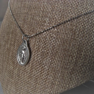 Puede incluir: Collar de cadena de plata con un colgante de plata con una imagen religiosa.