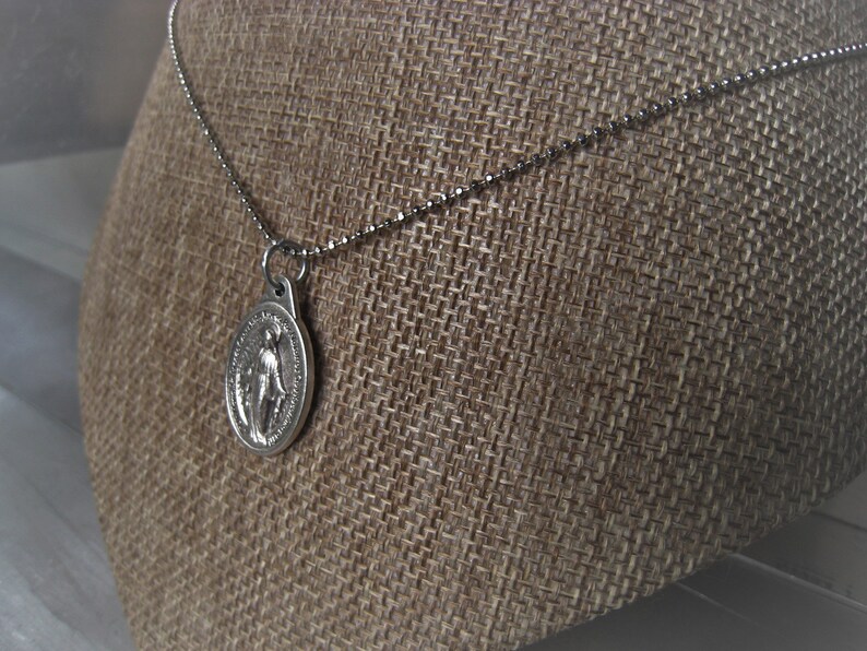 Puede incluir: Collar de cadena de plata con un colgante de plata con una imagen religiosa.