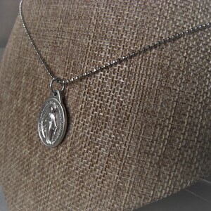 Puede incluir: Collar de cadena de plata con un colgante de plata con una imagen religiosa.