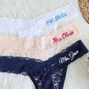 May include: Three embroidered lace thong underwear in white, peach, and navy blue. Each thong features a different name embroidered in a contrasting color: "Mrs. Stella", "Mrs. Olivia", and "Mrs. Grace".