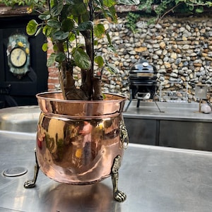 Maceta/jardinera antigua de cobre estilo Regencia con asas de máscara de león y patas de garra de león.