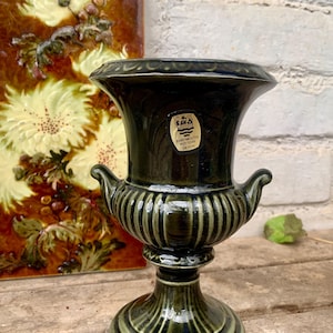 Może przedstawiać: Ciemnozielona ceramiczna waza z rozkloszowaną górą, dwoma małymi uchwytami i żebrowanym korpusem. Waza ma podstawę na cokole i błyszczące wykończenie. Etykieta na wazie głosi "Dartmouth Pottery Devon".