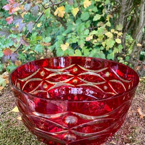 Può includere: Una ciotola di vetro rosso rubino con intricati motivi geometrici e a stella. La ciotola ha un design ampio e aperto. Il design della ciotola presenta una serie di forme e linee ripetute, creando un aspetto decorativo ed elegante.