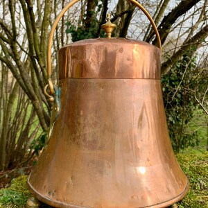 May include: A copper coal scuttle with a brass handle and lid. The scuttle has three brass feet and is sitting on a bed of moss.