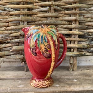 Puede incluir: Jarra de cerámica roja con ribete dorado y un diseño de palmera pintado.
