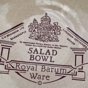 Puede incluir: Un bol de ensalada de cerámica blanca con un diseño en blanco y negro. El diseño presenta un escudo de armas real, las palabras "Royal Barum Ware" y el texto "By appointment Pottery Makers to Her Majesty Queen Elizabeth the Queen Mother".