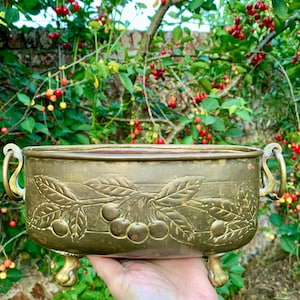 Può includere: Un'antica fioriera in ottone di forma rettangolare, con disegni a rilievo di rami di ciliegio. La fioriera ha manici ornati e poggia su piccoli piedini decorativi. L'ottone ha una calda patina invecchiata.