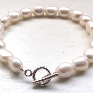 Könnte beinhalten: Ein Armband aus weißen Perlen mit einem silbernen Toggle-Verschluss.