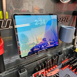 May include: A tablet displaying the time 2:34 is mounted on a garage wall. The tablet's screen shows a colorful abstract image. Various tools, including sockets and wrenches, are organized below the tablet.