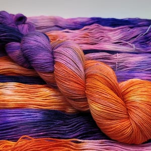 May include: A white ceramic mug with a black handle and the text "But First, Coffee" in a bold, black font. The mug is set against a blurred background, suggesting a cozy setting.