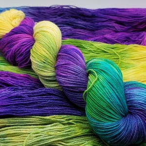 May include: Close-up of colorful yarn skeins in shades of yellow, purple, green, and blue. The yarn is arranged in a visually appealing pattern, showcasing the vibrant color variations. Ideal for knitting and crochet projects.
