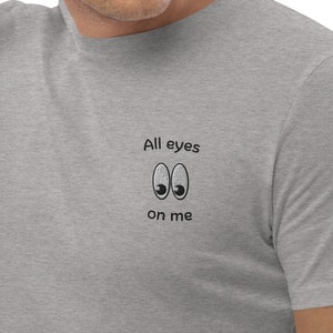 Könnte beinhalten: Ein hellgraues T-Shirt mit dem Text "All eyes on me" und zwei Comic-Augen.