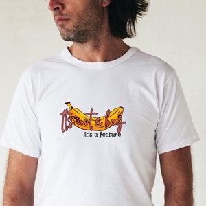 Peut inclure: T-shirt blanc avec un motif de banane jaune et le texte "Ce n'est pas un bug, c'est une fonctionnalité".