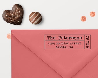 May include: A coral pink envelope featuring a black rectangular stamp with the text The Petersons, 14376 Madison Avenue, Austin, TX, and the zip code 78729. The envelope is decorated with small copper-colored circular confetti pieces.