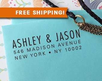 Puede incluir: Tarjeta azul claro con los nombres "ASHLEY & JASON" y detalles de la dirección en fuente negra. Un cordón de cuero negro con una cadena y un anillo dorados está unido a la tarjeta. Una pancarta naranja con "FREE SHIPPING!" en la parte superior.