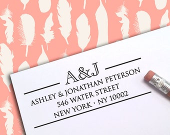 May include: A white card with black text, including the names "Ashley & Jonathan Peterson" and an address. The card is partially visible, with a pencil in the corner. The background features a pattern of white feathers on a coral background.