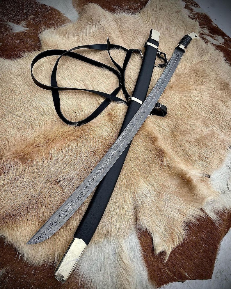 May include: A black leather scabbard with a silver-coloured metal hilt and a long, curved, silver-coloured blade with a damascus pattern. The sword is lying on a brown and white fur surface.