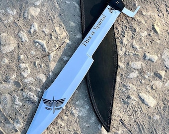 May include: A silver sword with a black handle and a leather sheath. The sword has the words "This is Sparta!" engraved on the blade and a logo for "Model Knives" on the bottom.