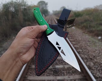 May include: A stainless steel knife with a green handle and a black leather sheath. The knife blade has a unique geometric design. The sheath is stitched with red thread. The text "MODEL KNIVES" is visible on the sheath.