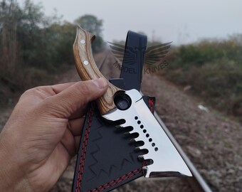 May include: A stainless steel knife with a wooden handle and a black leather sheath. The knife blade has a unique saw-tooth design. The sheath is stitched with red thread. The handle is made of light brown wood.