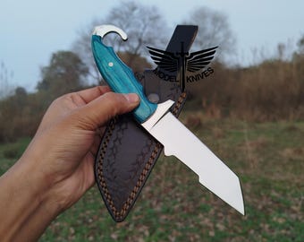 May include: A stainless steel knife with a turquoise wooden handle and a curved top. The knife is in a brown leather sheath. The text "MODEL KNIVES" is visible on the sheath.
