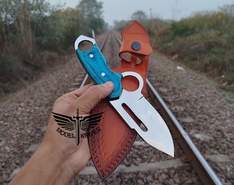 May include: A stainless steel knife with a blue handle and a brown leather sheath. The knife has a curved blade and a hole in the handle. The sheath has a belt loop and a snap closure. The text "MODEL KNIVES" is visible.