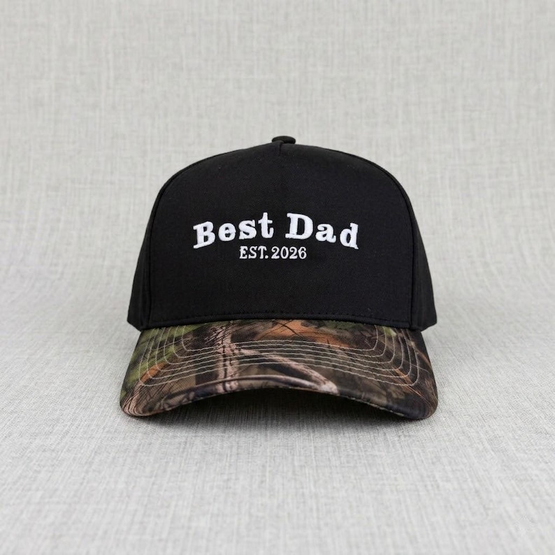 May include: Black baseball cap with a camouflage brim. The cap features the white text "Best Dad" above "EST. 2026". The hat is a classic six-panel design with a curved brim and adjustable strap.