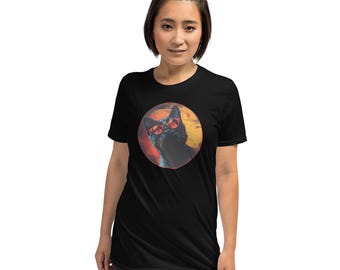 May include: A black short-sleeved t-shirt featuring a circular graphic on the chest. The graphic depicts a black cat wearing red-tinted sunglasses, set against a warm-toned sunset background with orange and yellow hues and a small sun.