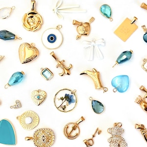 May include: An assortment of gold-tone charms with various designs, including a heart, an anchor, a flower, an eye, a crab, a shoe, a teddy bear, a fleur-de-lis, a butterfly, a star, a key, a scale, an elephant, a seashell, and a 'Love You' inscription. The charms are displayed on a white background.