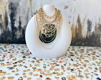 May include: A white display stand with a variety of gold chain necklaces. The stand is surrounded by a large collection of gold charms and pendants.