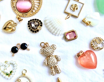 May include: Assortment of gold-tone charms with various designs, including a heart, a bear, sunglasses, a seashell, a flower, and a crystal. The charms are on a white background.